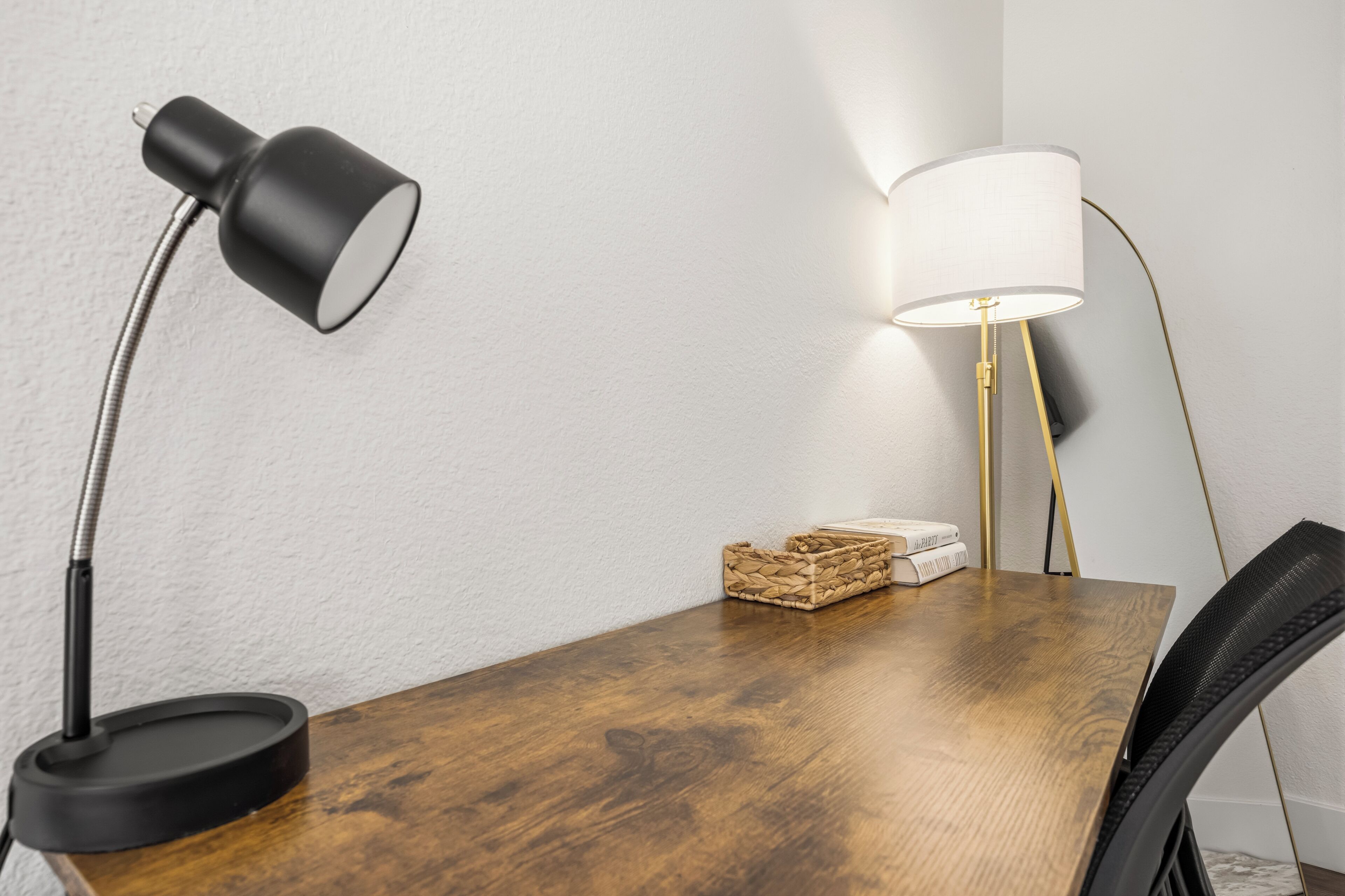 A wooden table with a black desk lamp and a floor lamp with a white shade.