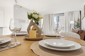 Una mesa de comedor dispuesta con platos, cubiertos, copas de vino, una vela y un florero decorativo con flores.