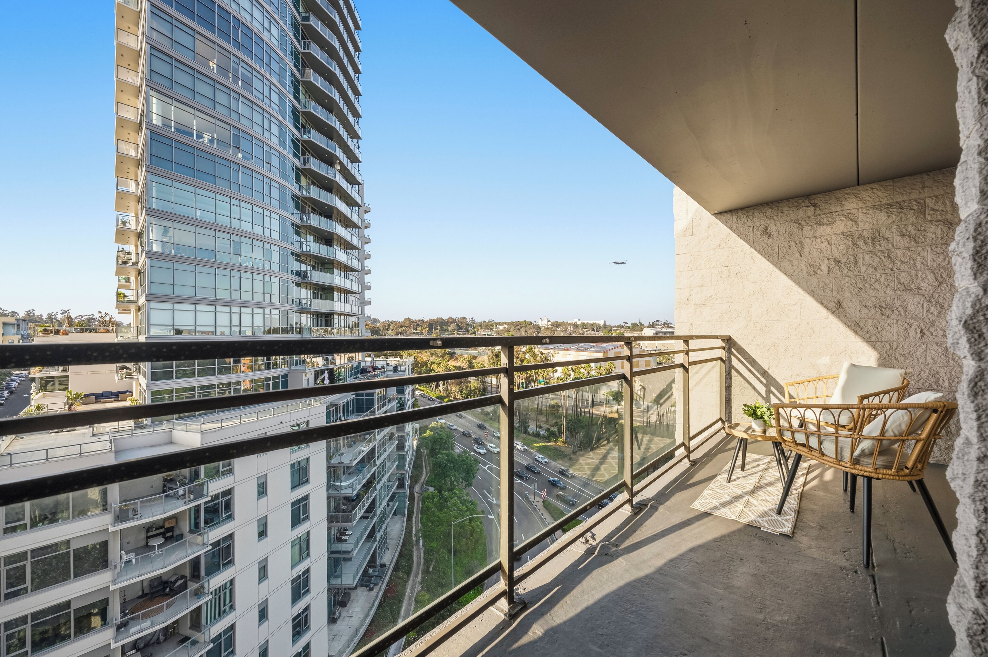 A balcony with a view of a tall building, a road, and a plane in the distance.