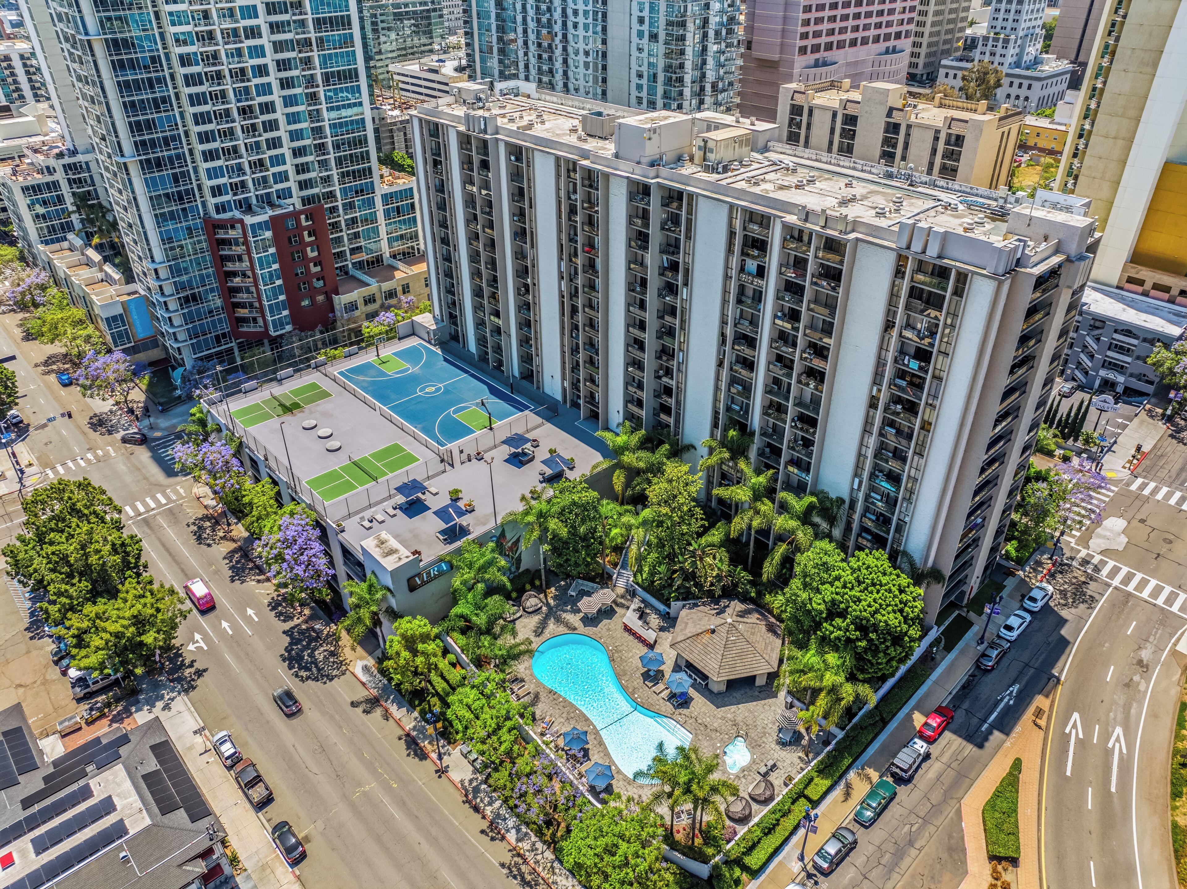 A high-rise building with a rooftop pool, tennis courts, and a small pavilion.
