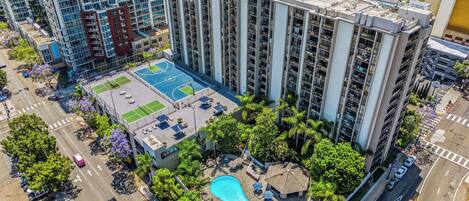 A high-rise building with a rooftop pool, tennis courts, and a small pavilion.