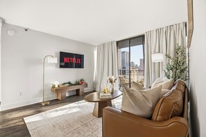 Uma sala de estar moderna com sofá, mesa de centro e uma TV exibindo 'NETFLIX' na parede.
