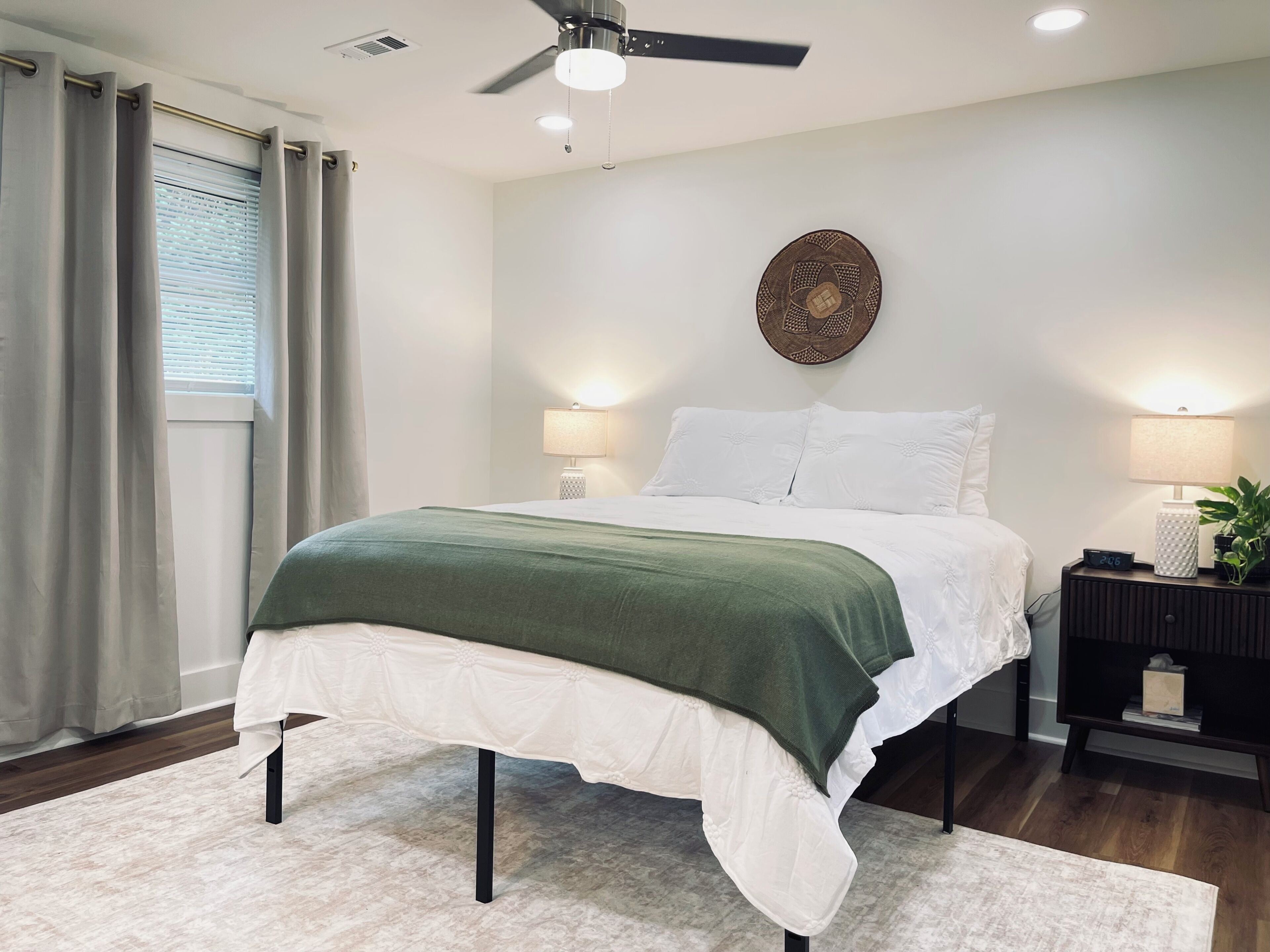 Une chambre à coucher comprenant un lit, des tables de chevet, un ventilateur de plafond et un élément décoratif fixé au mur.