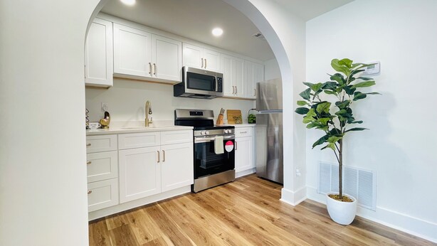 A modern kitchen with white cabinets, stainless steel appliances, and a wooden floor.