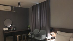 Een hotelkamer met een bed, een bureau met stoel, een tafeltje, een spiegel en een raam met gordijnen.
