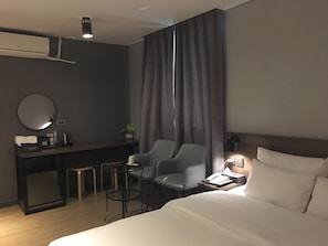 A hotel room with a bed, a desk with a chair, a small table, a mirror, and a window with curtains. - MOMO Hotel (Seoul)