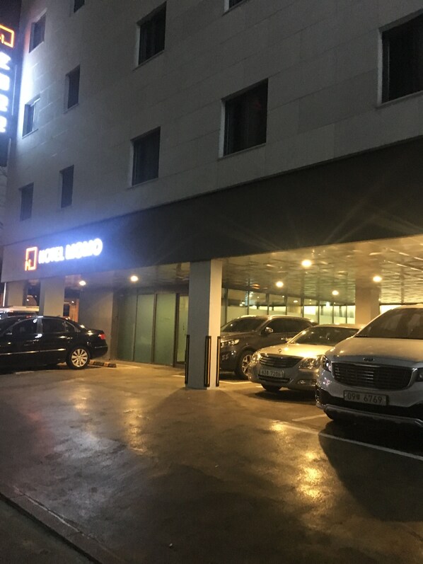 A hotel entrance with a sign, a covered parking area, and several parked cars. - MOMO Hotel (Seoul)