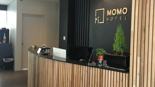 Een receptiebalie met zwart en houten design, een receptiegedeelte en een bord met de tekst Momo Hotel.