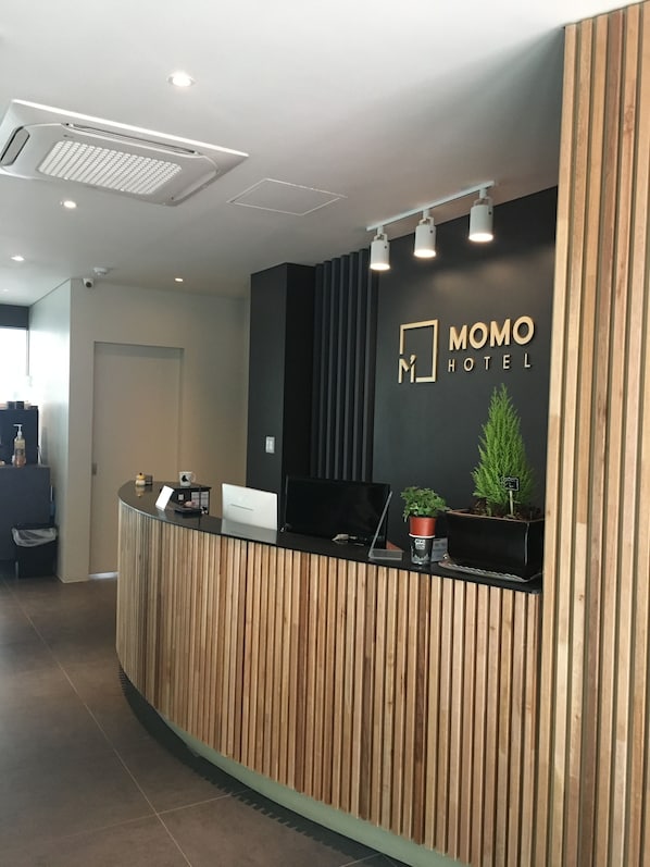 En receptionsdisk med en svart och träfärgad design, ett receptionsområde och en skylt för Momo Hotel.