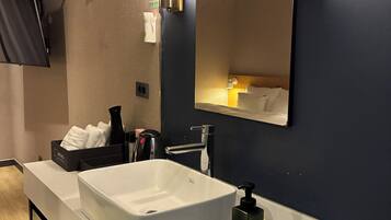 A modern hotel bathroom with a large mirror, a white sink, and a black soap dispenser.