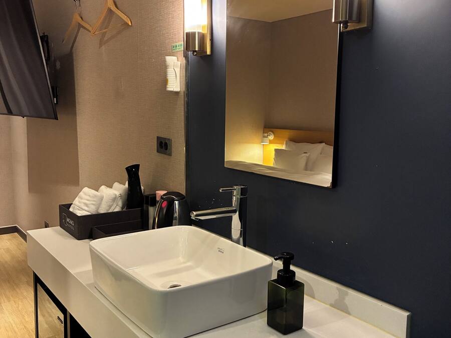 A modern hotel bathroom with a large mirror, a white sink, and a black soap dispenser.