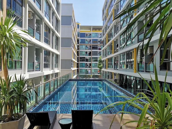 Ein modernes Hallenbad mit klarem, blauem Wasser, umgeben von mehrstöckigen Gebäuden mit Balkonen und großen Fenstern.