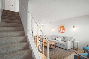Eine Treppe führt zu einem Wohnbereich mit einer Couch, einem Couchtisch und einem kleinen Beistelltisch.