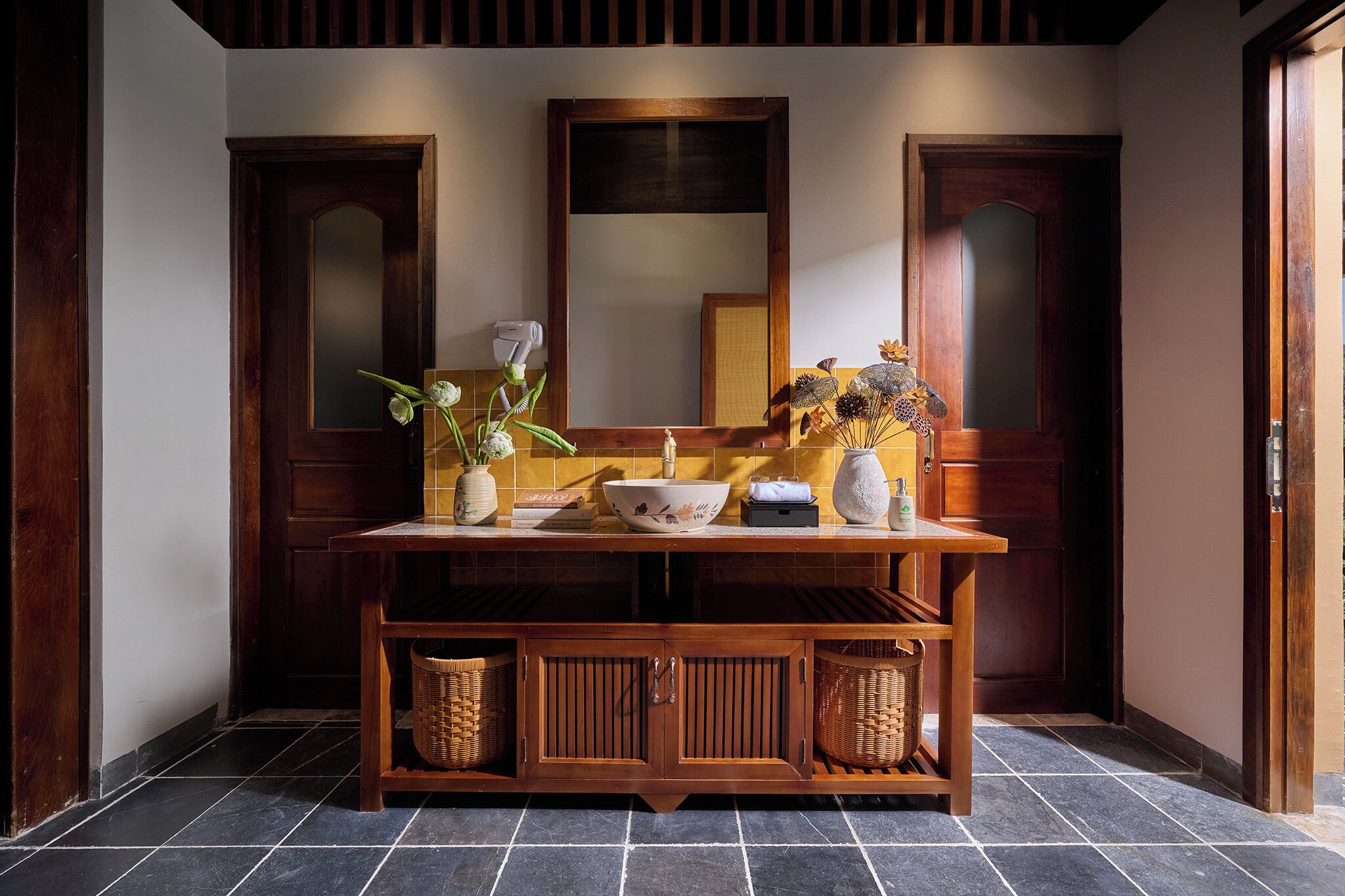 A wooden vanity with a mirror, a bowl, and two vases with flowers.