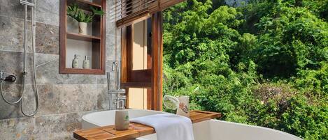 A modern bathroom with a freestanding bathtub, a shower, and a window with a view of lush greenery.