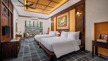 A hotel room with two beds, a ceiling fan, a stone wall, and a television.