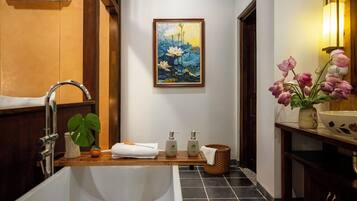 A bathroom with a bathtub, a sink, a mirror, a painting of flowers, and a vase with flowers.