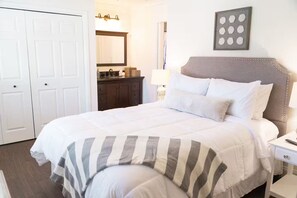 A bedroom with a bed, a dresser, a nightstand, a mirror, and a wall-mounted picture. - Harbor Home (Oldsmar)