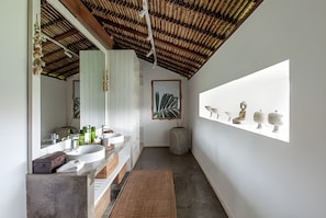 A modern bathroom with a large mirror, white sink, and a concrete bench.