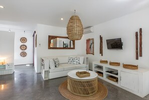 A modern living room with a white sofa, a round coffee table, a hanging woven light fixture, a flat-screen TV, and decorative wall art.
