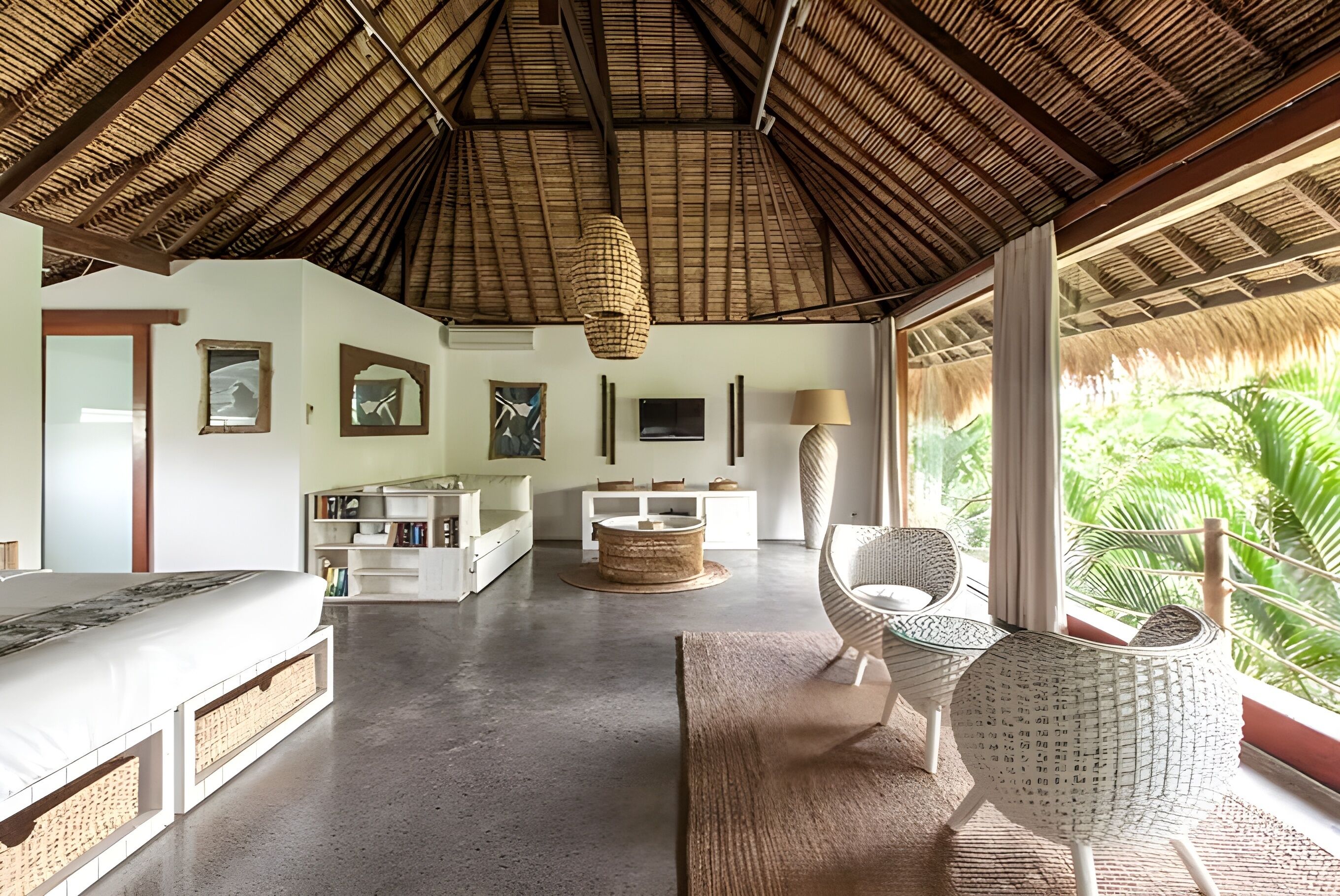 A spacious room with a thatched roof, a bed, a sofa, a dining table, and a chair.