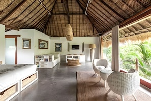 A spacious room with a thatched roof, a bed, a sofa, a dining table, and a chair.