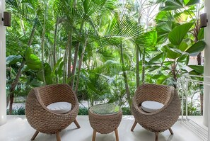 A room with three wicker chairs and a small table, surrounded by lush green plants. - Kima Surf Camp Canggu (Canggu)