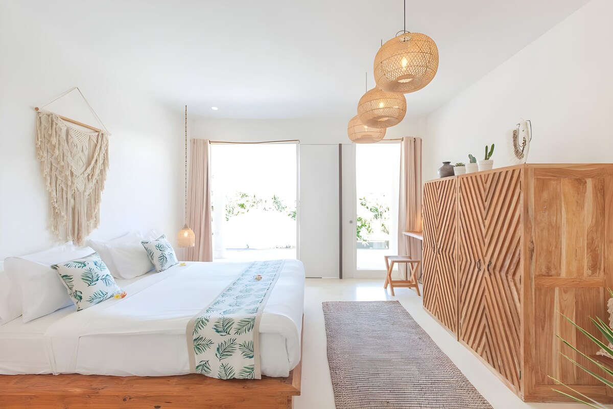 Quarto moderno com uma cama grande, guarda-roupa de madeira, um painel de macramé e uma janela ampla com vista para o verde.