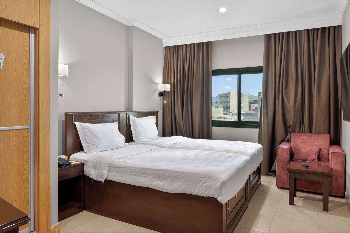 A hotel room with a large bed, a desk, a chair, and a window with curtains.