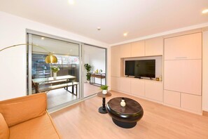 Un salon moderne comprenant un canapé, une table basse, un téléviseur et une porte-fenêtre coulissante donnant sur un balcon.