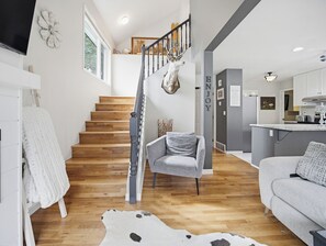 A modern interior with a wooden staircase, a grey sofa, a cowhide rug, and a kitchen area.