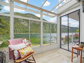 A room with a large window overlooking a lake, a rocking chair, and a small table with a basket.