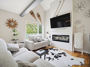 A modern living room with a fireplace, a large TV, and a view of a lake.