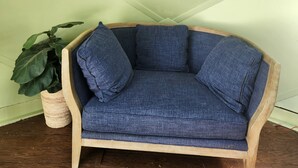 A blue upholstered sofa with wooden armrests and a woven basket with a plant beside it. - Peaceful country rustic glamping cottage- stargazing and mountain views (Saltville)