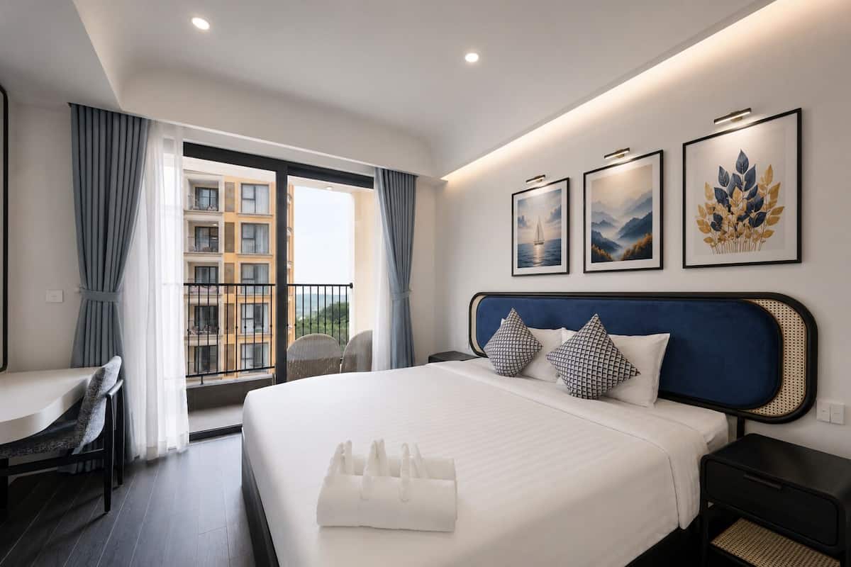 Habitación de hotel con cama, escritorio, silla y vistas a edificios a través de una ventana.