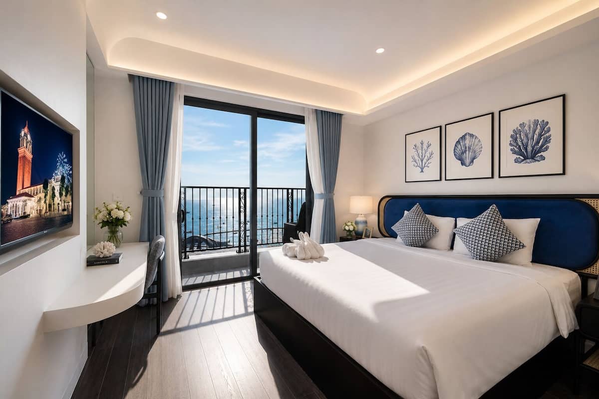 Habitación de hotel con cama, escritorio, televisión y balcón con vista al mar.