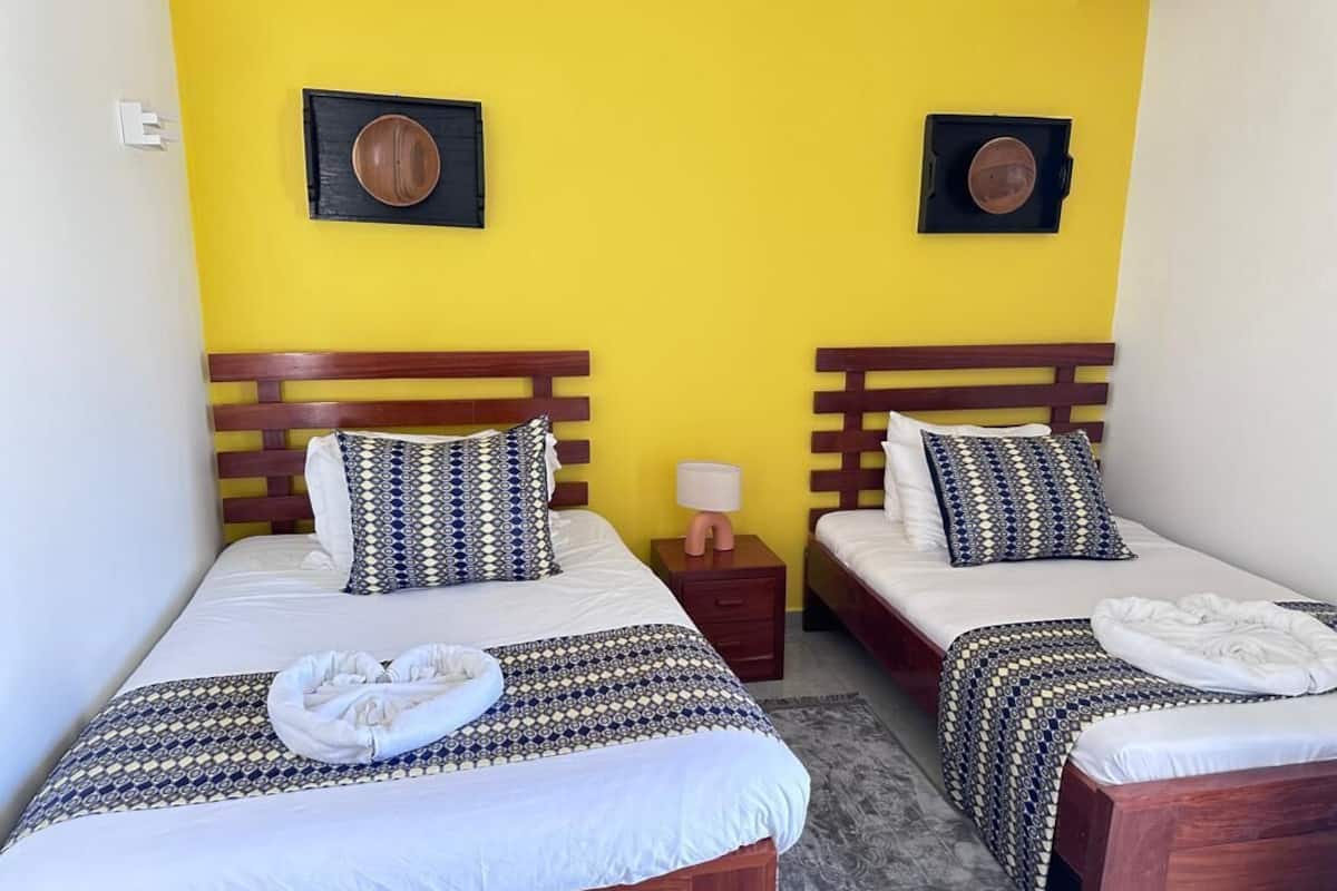 Two single beds with wooden headboards, a small bedside table with a lamp, and a wall-mounted decorative plate.