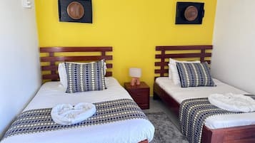 Dos camas individuales con cabeceros de madera, una mesita de noche con lámpara y un plato decorativo colgado en la pared.