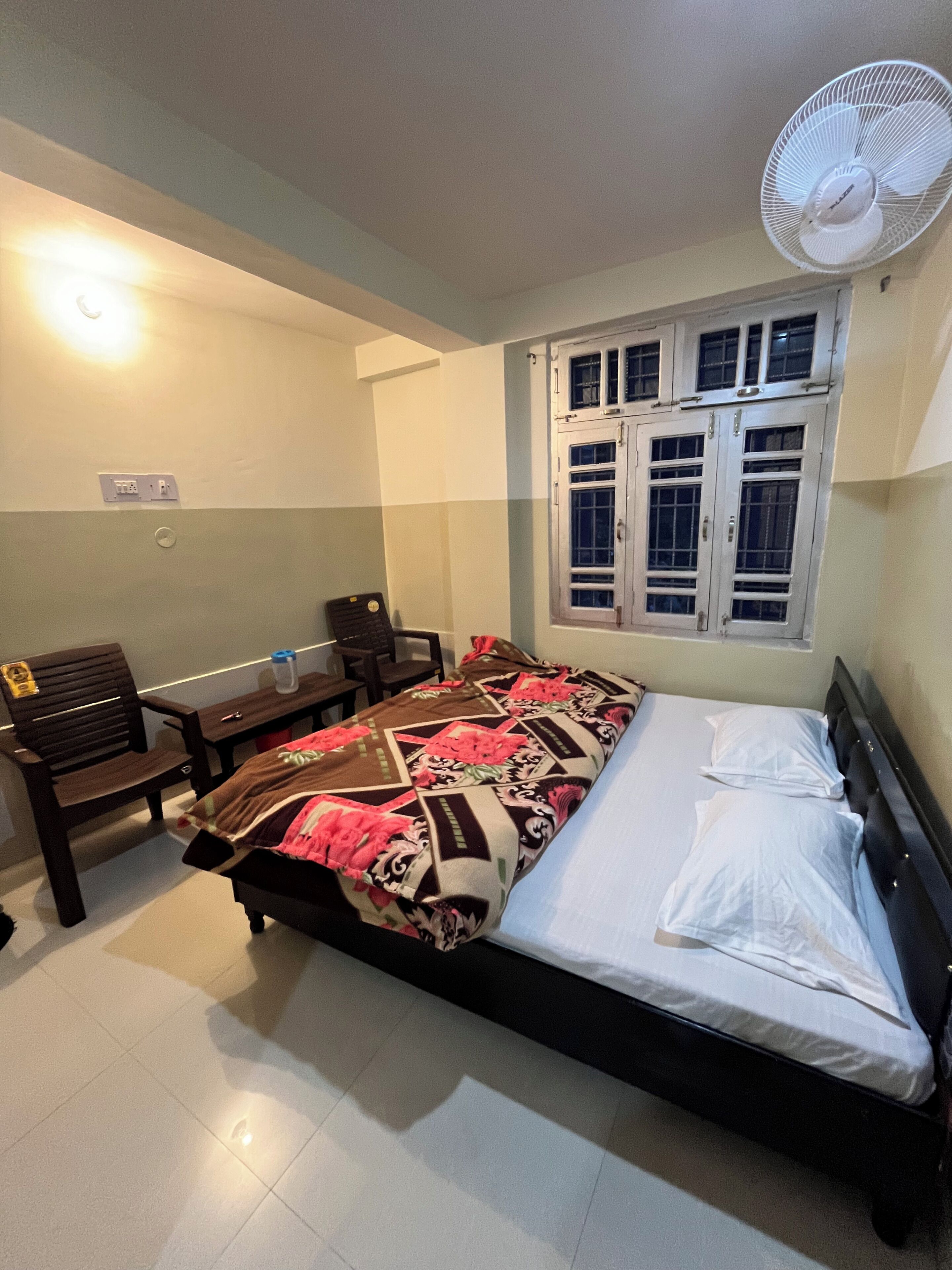 Une chambre à coucher comprenant un lit, un bureau, une chaise, une fenêtre avec des volets et un ventilateur de plafond.