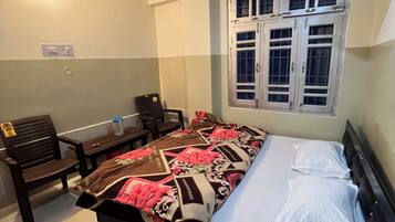 Une chambre à coucher comprenant un lit, un bureau, une chaise, une fenêtre avec des volets et un ventilateur de plafond.