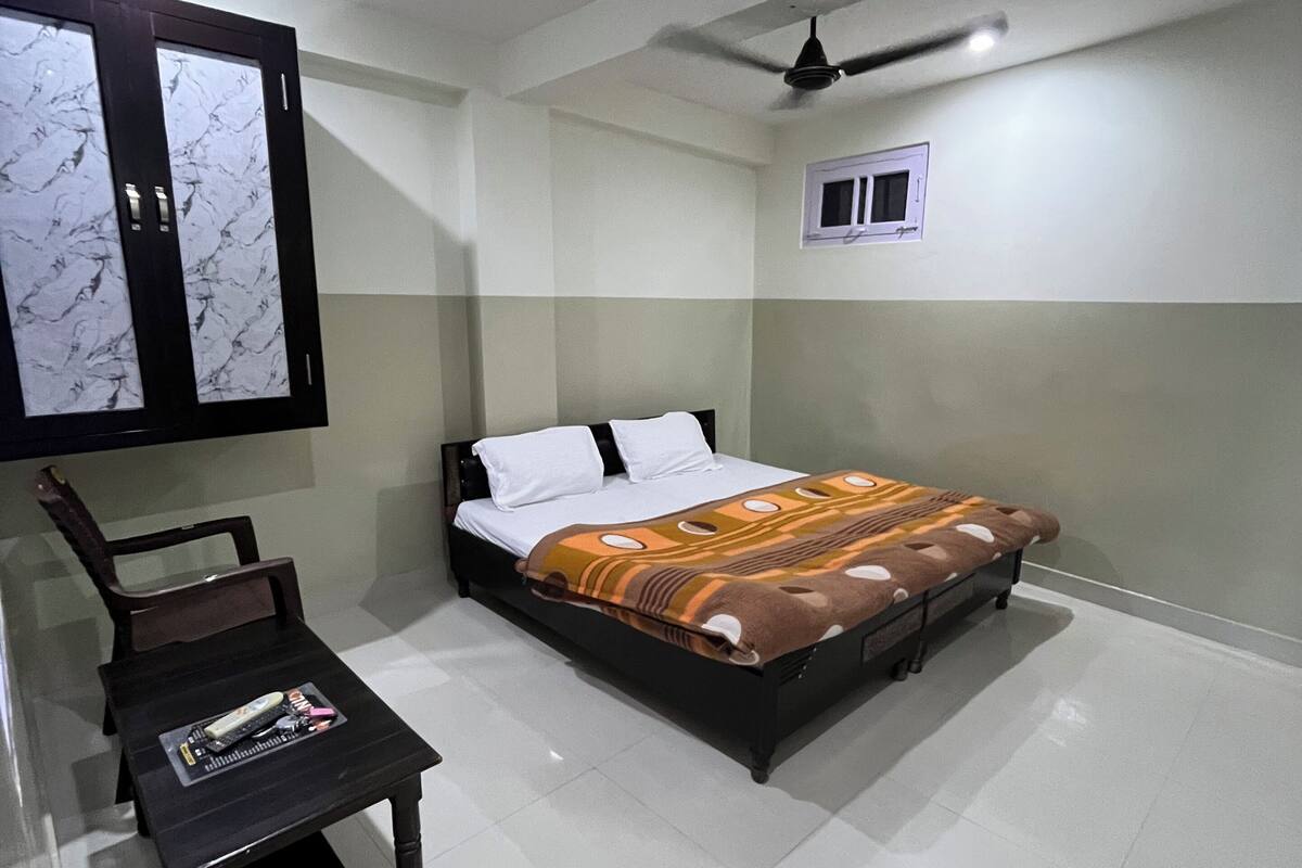 Une chambre à coucher avec un lit, une petite table, une chaise, un ventilateur de plafond et une fenêtre.