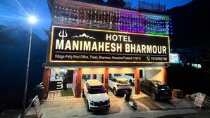 A hotel named 'Manimahesh Bharmour' with a signboard, a parking area with cars, and a mountainous backdrop. - Hotel Manimahesh Bharmour (Brahmaur)