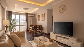 Uma sala de estar moderna com sofá, TV, área de refeições e janelas amplas.