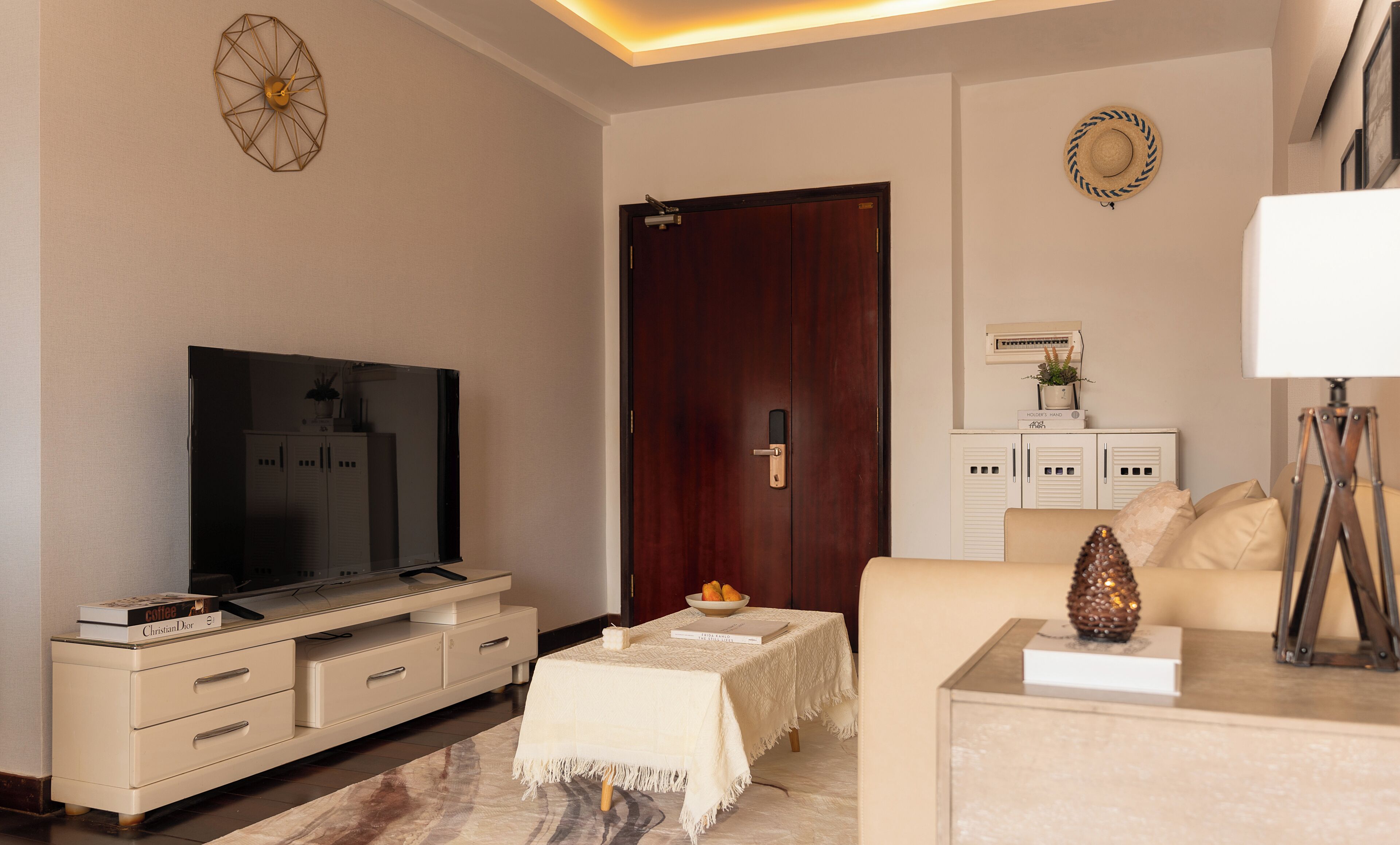 Een woonkamer met een televisie, een houten deur, een witte kast, een bank en een lamp.