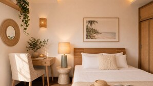Quarto de hotel com cama, mesa de cabeceira, abajur, cadeira e uma fotografia emoldurada de uma praia.