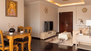 Uma sala de jantar com uma mesa de madeira, cadeiras, um vaso com flores, uma televisão, um armário e um sofá.