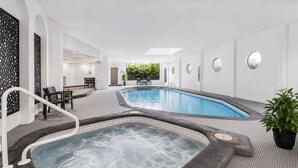 Een wellnessruimte met twee whirlpools en een zwembad, omringd door een betegelde vloer en witte wanden.