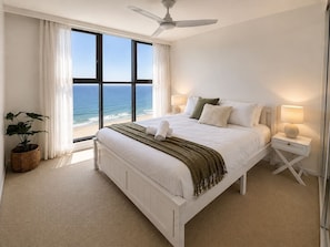 A bedroom with a large bed, a ceiling fan, a nightstand with a lamp, a potted plant, and a view of the ocean. - Beach Stay | 2 Car Parks, 2BR, Tennis Spa Sauna (Surfers Paradise)