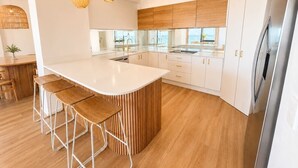 Een moderne keuken met een centraal eiland, barkrukken, hanglampen en witte kasten.