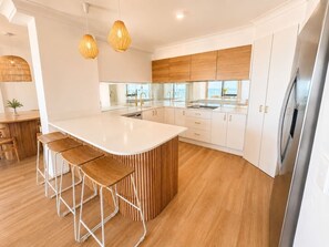 A modern kitchen with a central island, bar stools, pendant lights, and white cabinetry. - Beach Stay | 2 Car Parks, 2BR, Tennis Spa Sauna (Surfers Paradise)